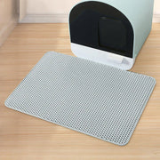 Un tapis alvéolé gris clair du lot Nidofé Alvéa, placé devant un bac à litière.